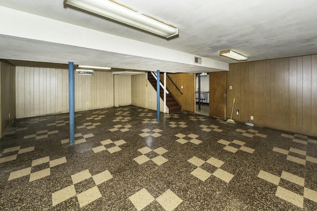 finished basement featuring stairway, visible vents, and wooden walls