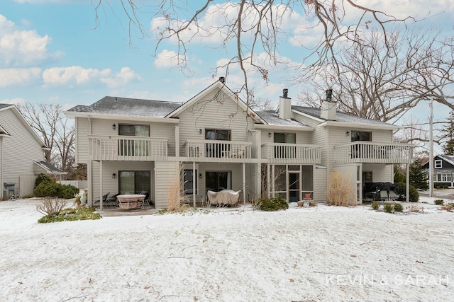 snow covered back of property featuring a chimney and a balcony