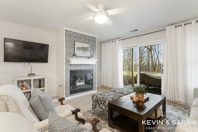 living area with a tiled fireplace, wood finished floors, visible vents, and a ceiling fan