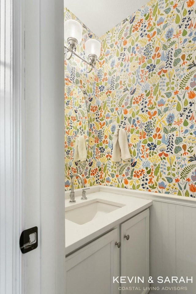 bathroom featuring a wainscoted wall, vanity, and wallpapered walls