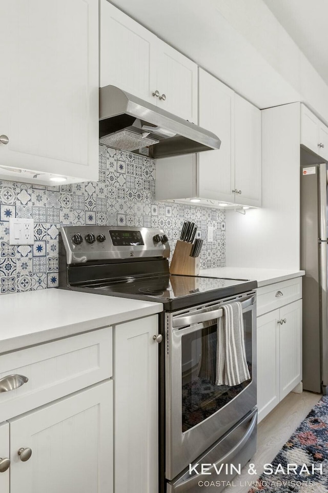 kitchen featuring under cabinet range hood, stainless steel appliances, white cabinetry, light countertops, and decorative backsplash