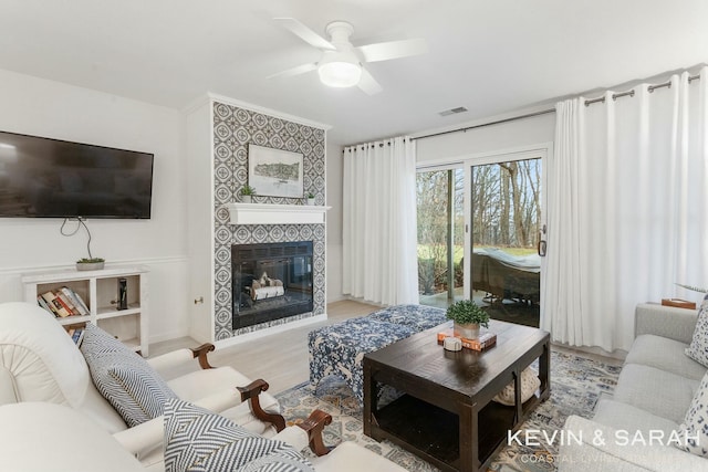 living area with ceiling fan, visible vents, a fireplace, and wood finished floors