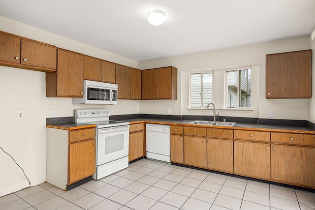 kitchen featuring brown cabinetry, dark countertops, white appliances, and a sink