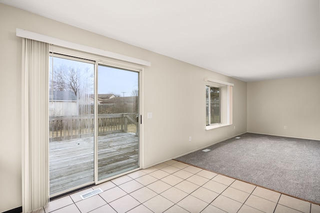 empty room featuring light tile patterned floors, visible vents, and light colored carpet