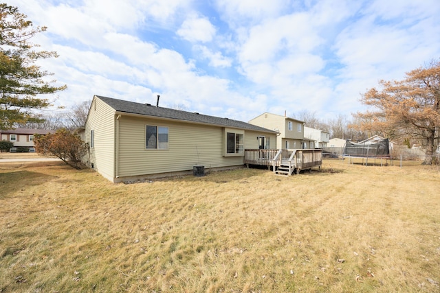 rear view of property featuring a deck, a trampoline, and a lawn