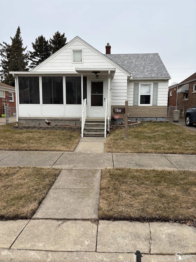 bungalow-style house featuring a sunroom, roof with shingles, a chimney, and a front lawn