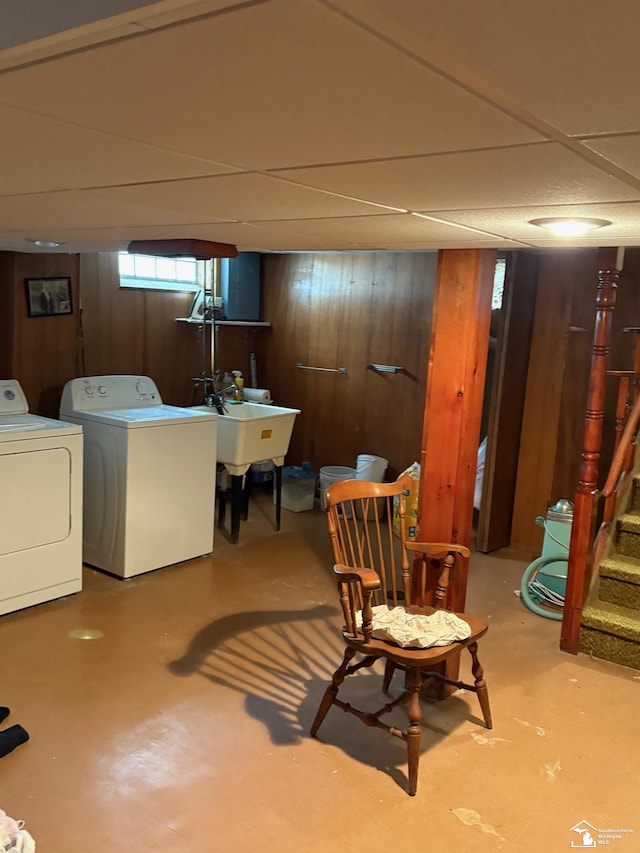 basement featuring a drop ceiling, wood walls, a sink, washer and dryer, and stairway