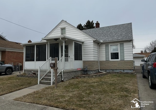 bungalow-style house with a shingled roof, a sunroom, stone siding, a front lawn, and a chimney