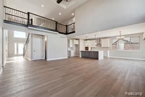 unfurnished living room featuring recessed lighting, ceiling fan with notable chandelier, a high ceiling, wood finished floors, and baseboards