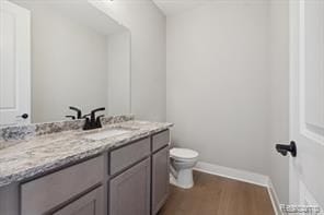 bathroom featuring toilet, baseboards, wood finished floors, and vanity