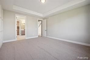 unfurnished bedroom featuring carpet floors, a raised ceiling, baseboards, and ensuite bathroom