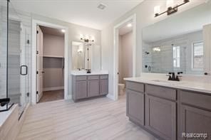 full bath featuring a shower stall, two vanities, a sink, and wood finished floors