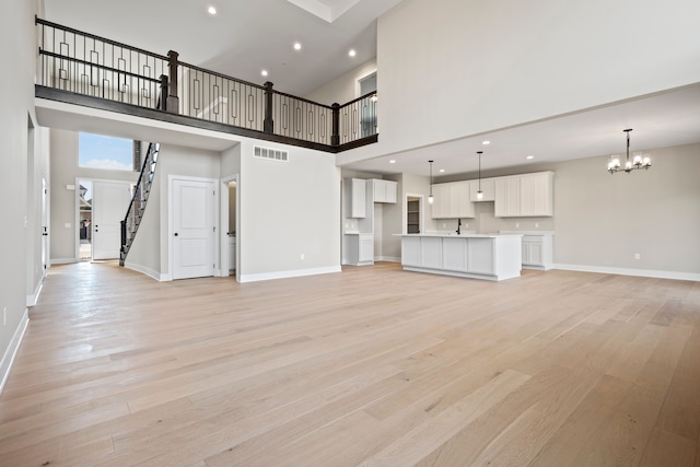 35689 Windridge Dr, New Baltimore, MI 48047 - unfurnished living room with visible vents, light wood-style floors, a high ceiling, and a chandelier