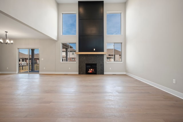 35689 Windridge Dr, New Baltimore, MI 48047 - unfurnished living room with a warm lit fireplace, an inviting chandelier, a high ceiling, baseboards, and light wood-type flooring