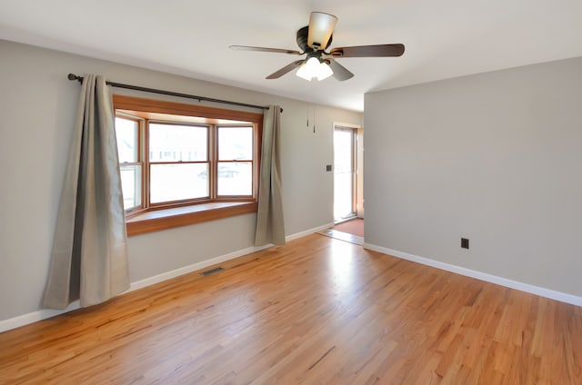 spare room featuring light wood finished floors, visible vents, a ceiling fan, and baseboards