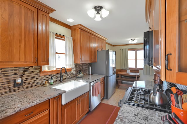 kitchen featuring a sink, backsplash, stainless steel appliances, brown cabinetry, and crown molding