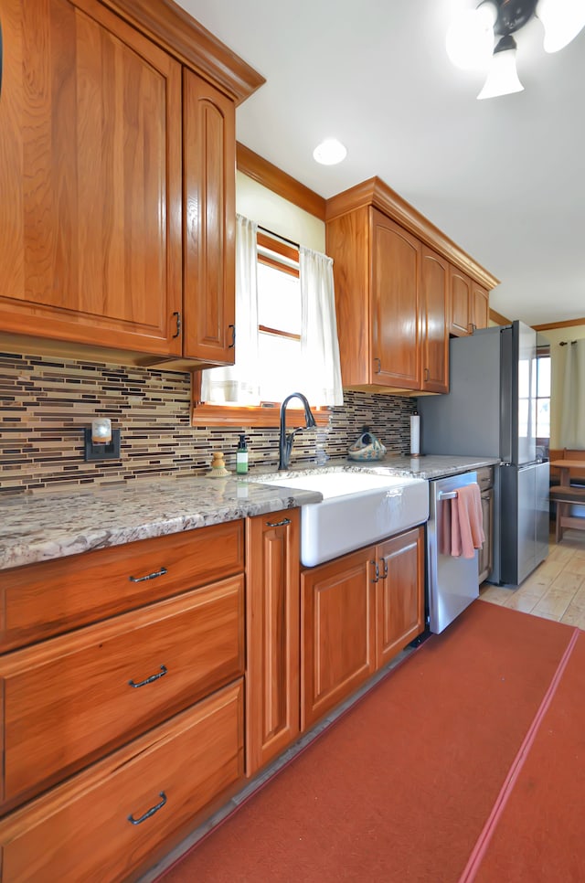 kitchen featuring a sink, brown cabinetry, decorative backsplash, light stone countertops, and dishwasher