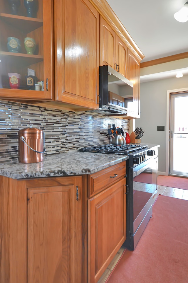 kitchen featuring stainless steel gas stove, backsplash, brown cabinetry, and light stone countertops