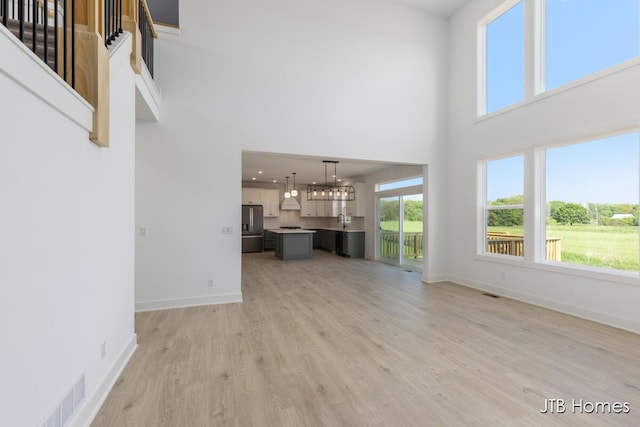 8123 Byron Depot Dr SW, Byron Center, MI 49315 - unfurnished living room with a towering ceiling, light wood-style flooring, baseboards, plenty of natural light, and a chandelier