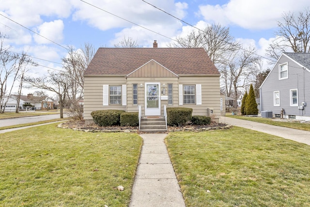 bungalow-style home with roof with shingles, a front lawn, a chimney, and central AC unit