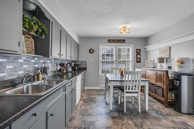 kitchen featuring a sink, baseboards, gray cabinets, backsplash, and dark countertops