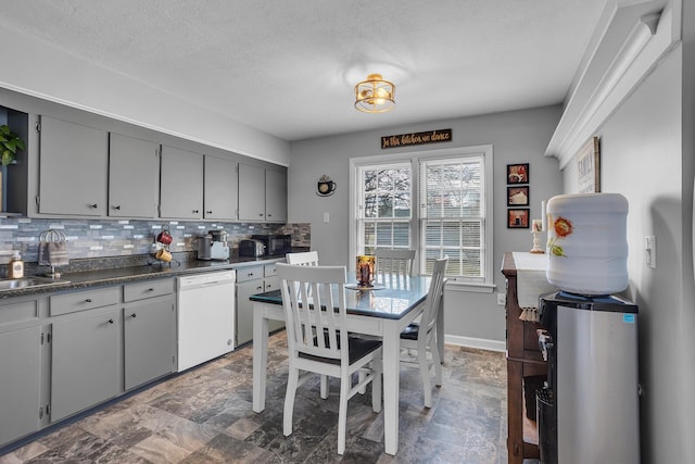 kitchen featuring tasteful backsplash, dark countertops, white dishwasher, gray cabinets, and a sink