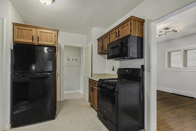 kitchen featuring baseboards, brown cabinets, light countertops, light wood-type flooring, and black appliances