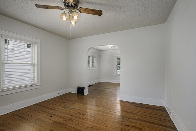 spare room featuring arched walkways, baseboards, a ceiling fan, wood-type flooring, and a textured ceiling