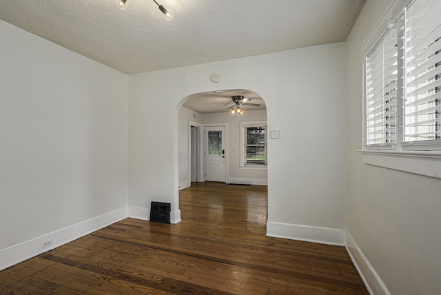 empty room featuring arched walkways, a textured ceiling, hardwood / wood-style flooring, and baseboards