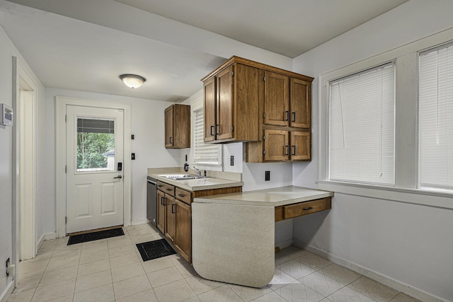 kitchen with a sink, baseboards, light countertops, dishwasher, and brown cabinetry