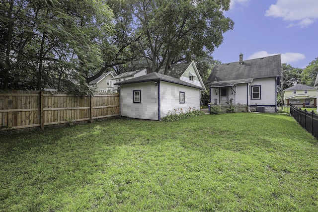 rear view of house with a fenced backyard, a yard, an outdoor structure, and central AC unit