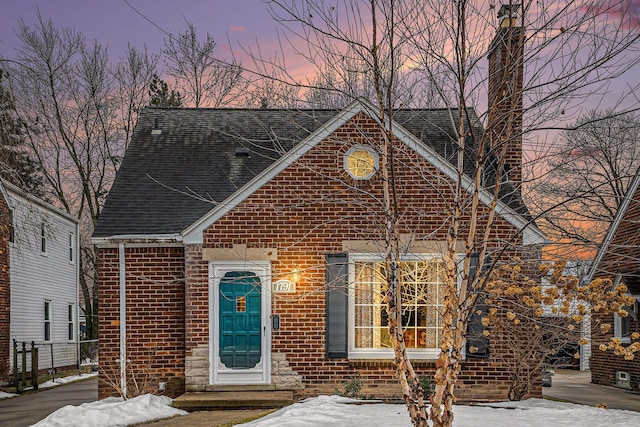 view of front of property featuring brick siding, a chimney, and a shingled roof