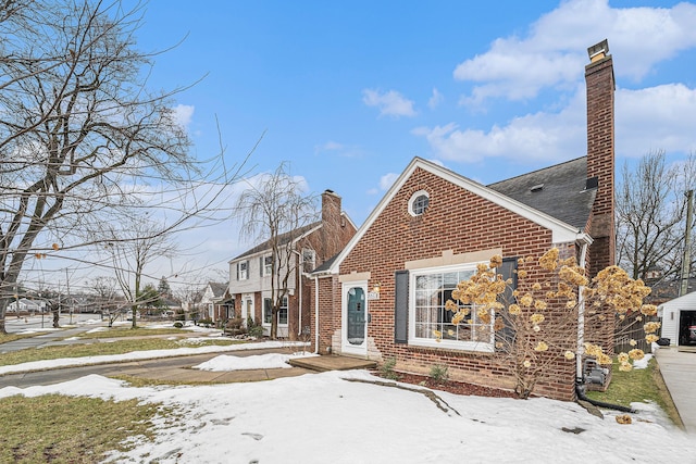 view of snowy exterior with brick siding and a chimney