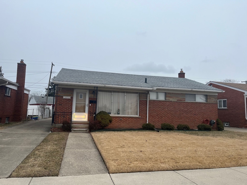 bungalow-style home with a front yard, brick siding, and roof with shingles