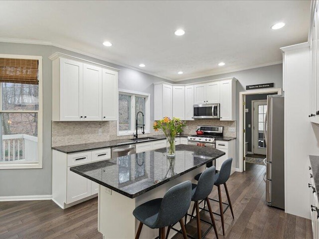 kitchen with appliances with stainless steel finishes, ornamental molding, dark wood-type flooring, a kitchen bar, and a sink