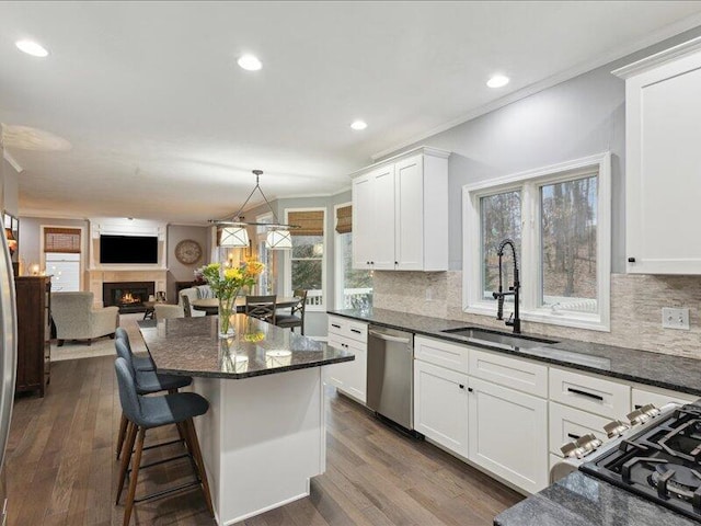 kitchen featuring dishwasher, a warm lit fireplace, a sink, and white cabinets