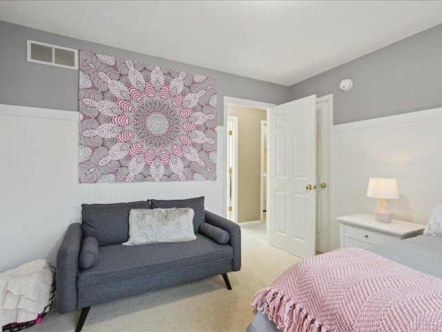 bedroom with a wainscoted wall, visible vents, and light carpet