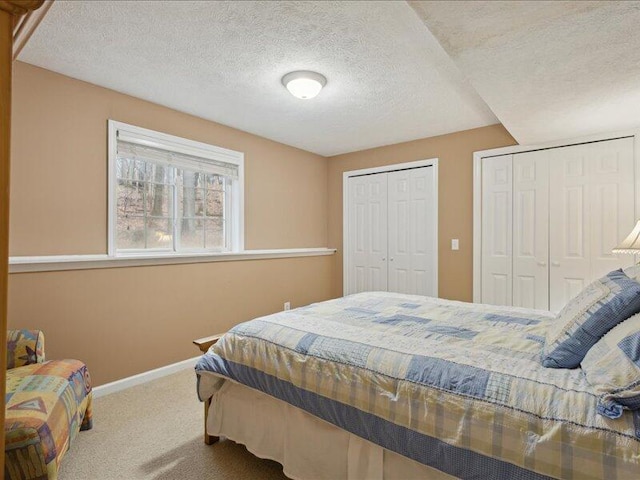 bedroom featuring carpet, a textured ceiling, baseboards, and multiple closets