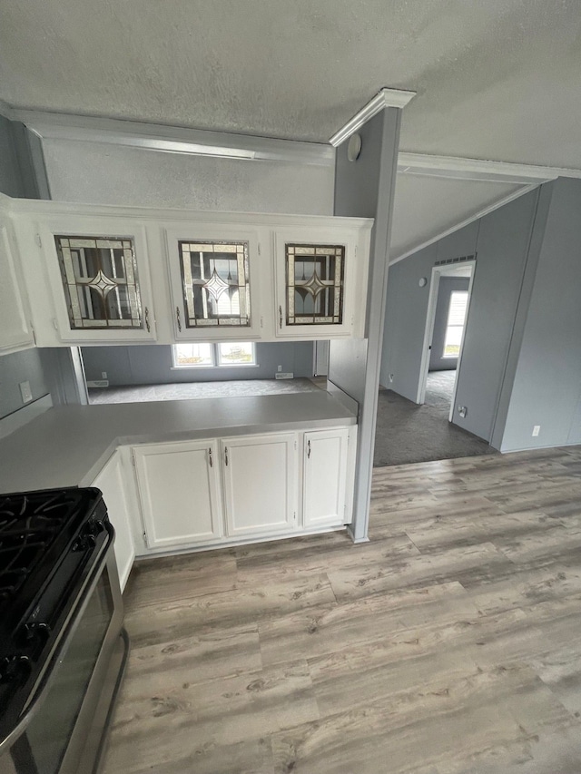 kitchen with stainless steel gas stove, white cabinets, light wood-style flooring, and a textured ceiling