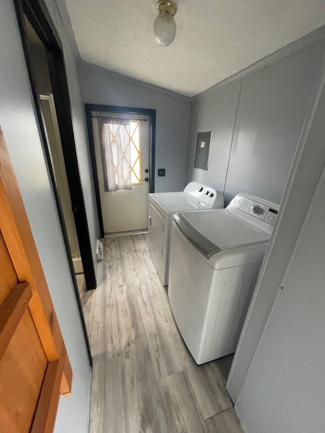 laundry room with light wood-style flooring, a textured ceiling, washer and dryer, laundry area, and electric panel