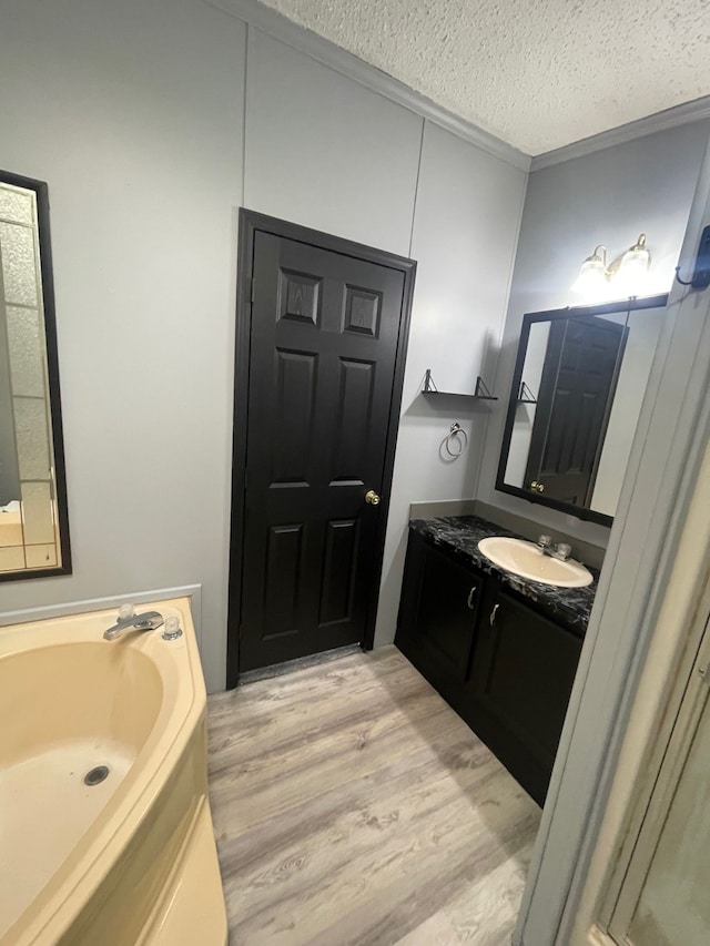 bathroom with a textured ceiling, wood finished floors, vanity, and a bath