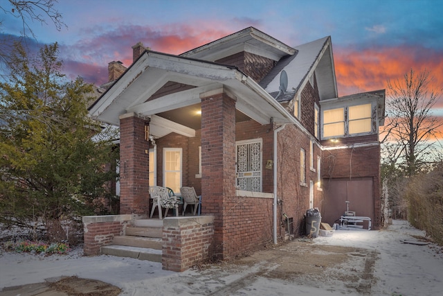 view of front of house with driveway, a porch, a chimney, and brick siding