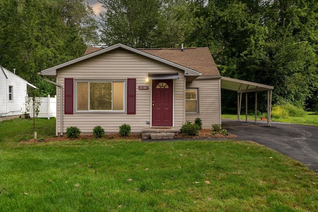 view of front facade featuring a shingled roof, aphalt driveway, fence, a carport, and a front yard