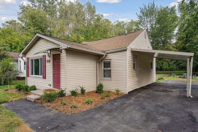 view of side of home featuring a shingled roof, aphalt driveway, and a carport