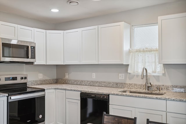 kitchen featuring appliances with stainless steel finishes, white cabinetry, a sink, and light stone counters