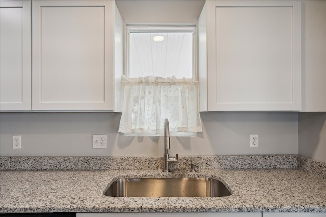 kitchen featuring white cabinetry, light stone counters, and a sink