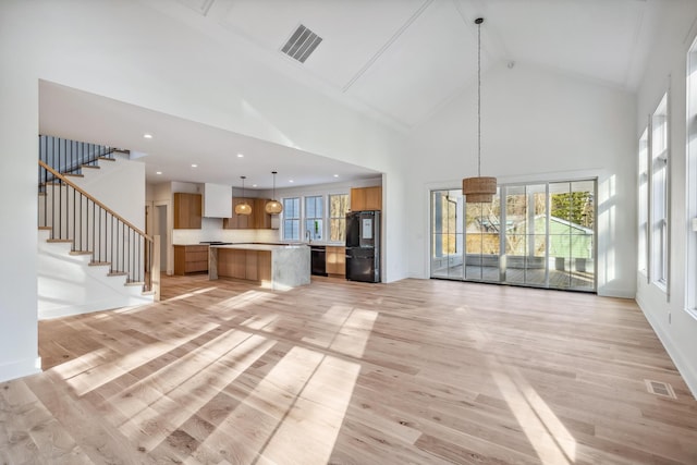 unfurnished living room with light wood-style floors, stairway, visible vents, and high vaulted ceiling