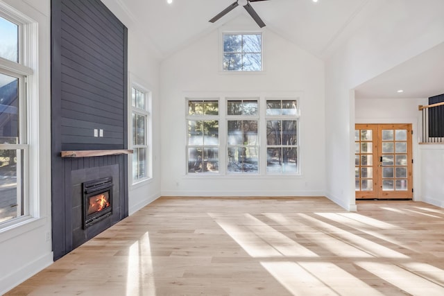 unfurnished living room with high vaulted ceiling, a fireplace, wood finished floors, and baseboards