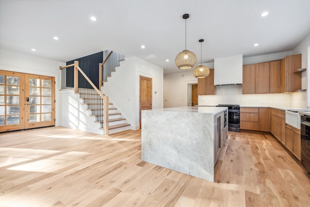 kitchen featuring stove, a center island, light wood finished floors, modern cabinets, and tasteful backsplash