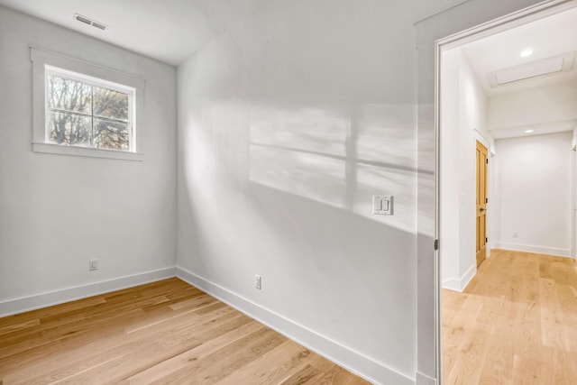 empty room featuring visible vents, light wood finished floors, attic access, and baseboards